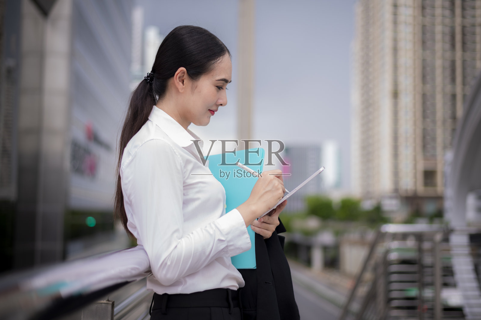 身穿西装的女商人站着,手中拿着平板电脑,显得自信且专注于她的工作,身处公共交通或旅行中心,走廊上有遮盖。照片摄影图片
