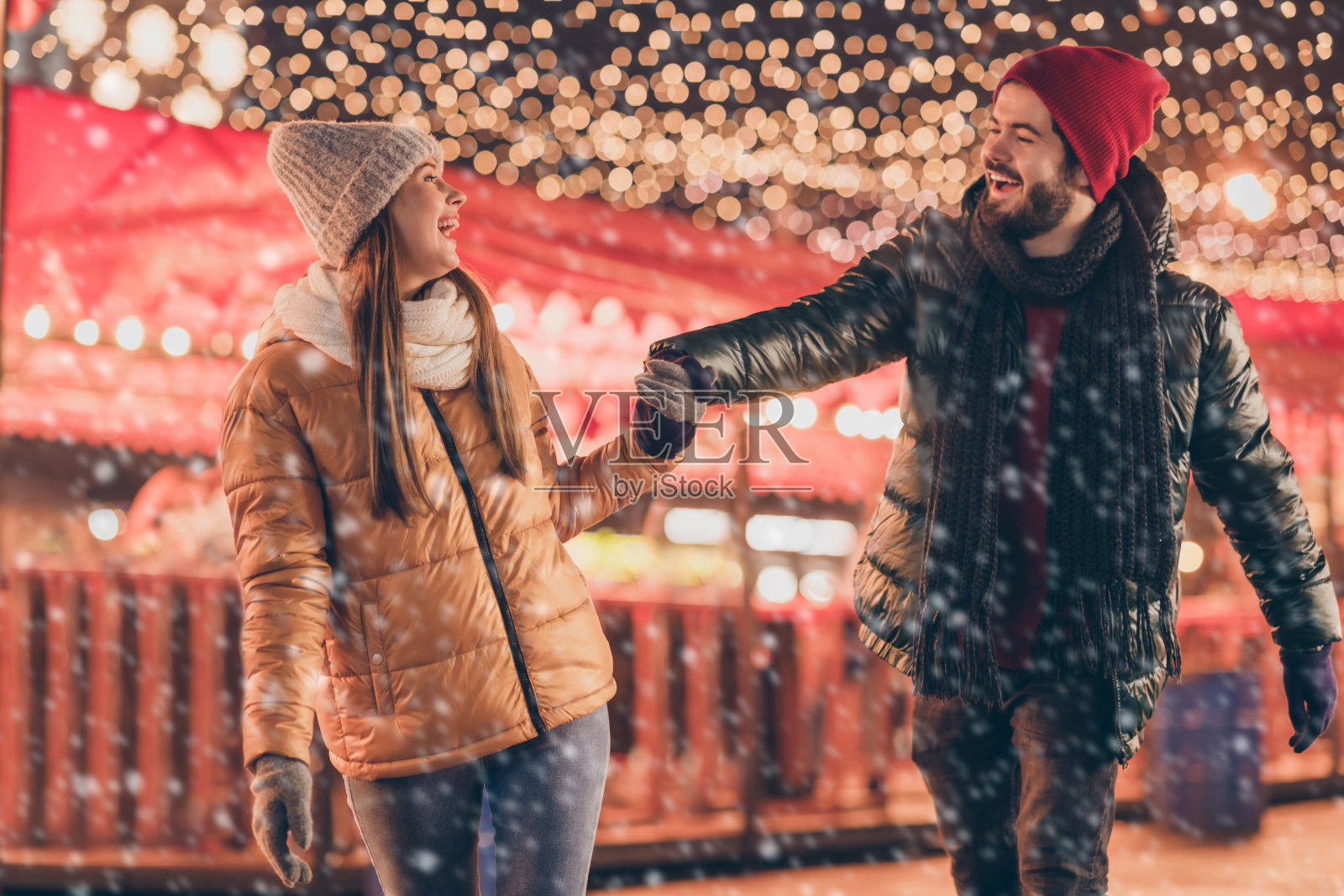 情侣在圣诞节的夜晚集市上手牵手,享受户外的灯光装饰,穿着季节性的外套。照片摄影图片