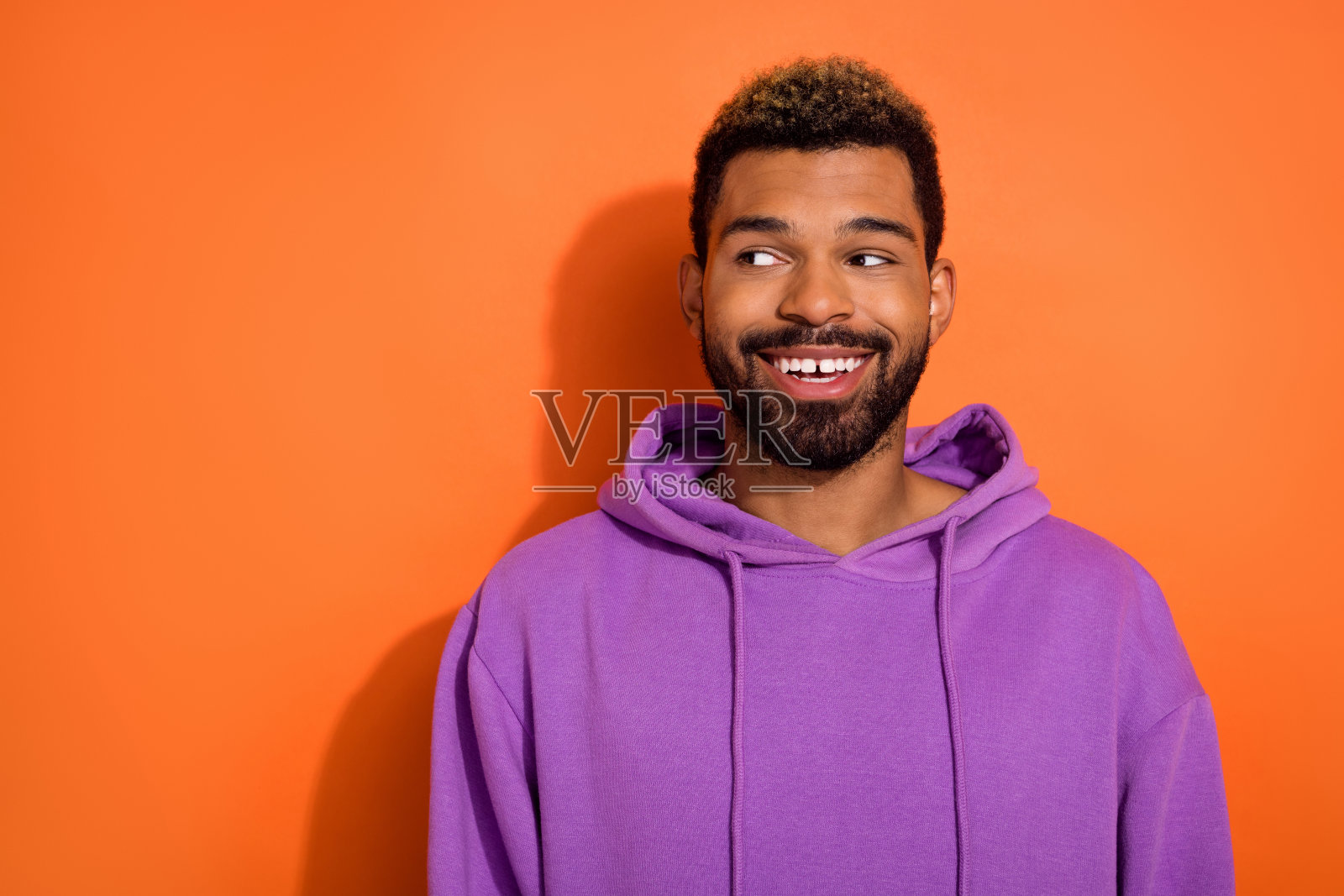 有趣的男孩穿着紫色卫衣,望着空旷的空间,想要给女朋友一个惊喜,背景为橙色。照片摄影图片