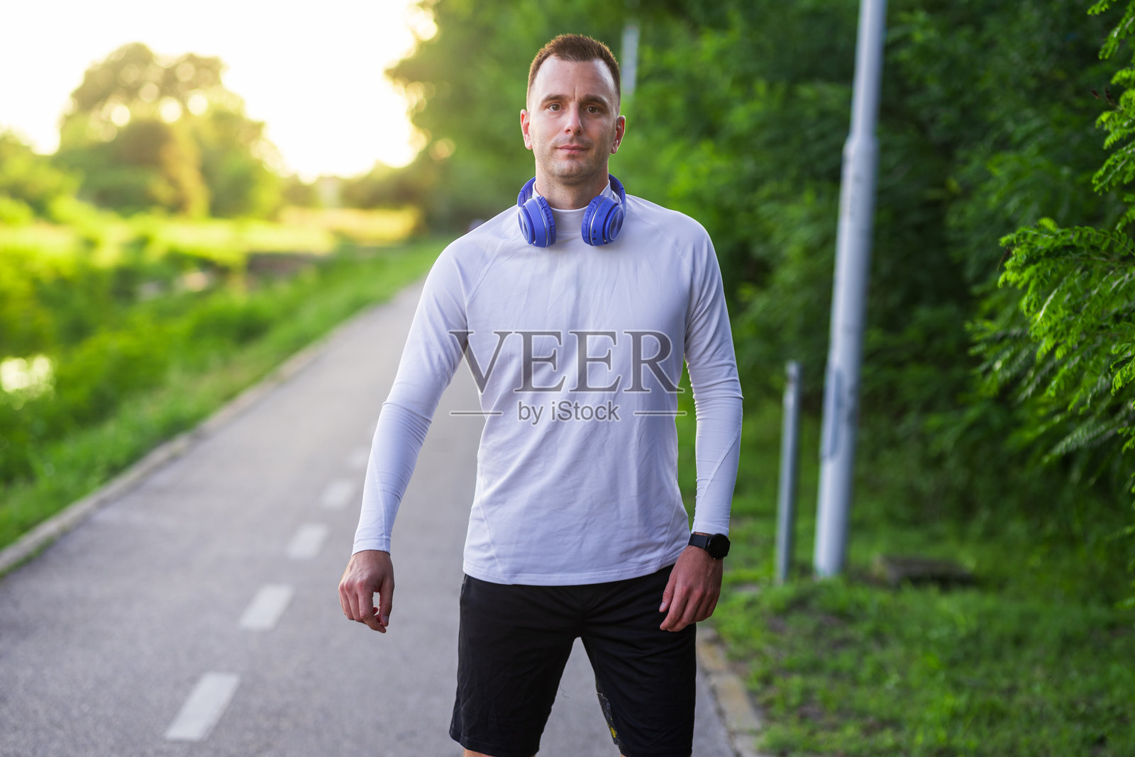 年轻运动员在训练后戴着耳机走在公园里照片摄影图片