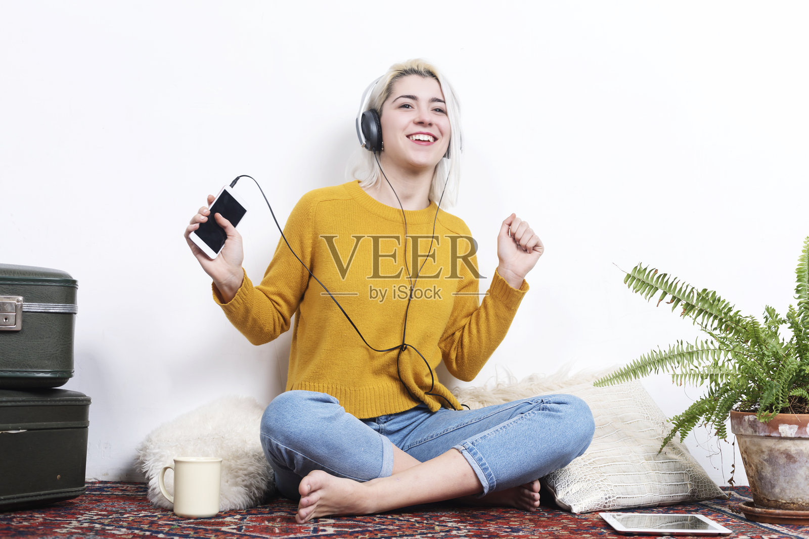 女人在舒适的房间里听音乐,轻触一株蕨类植物。照片摄影图片