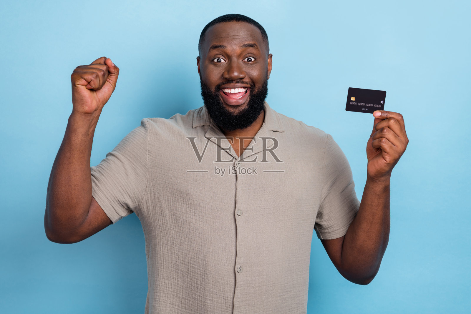 兴奋满意的人举起拳头,手持塑料借记卡,背景为蓝色。照片摄影图片