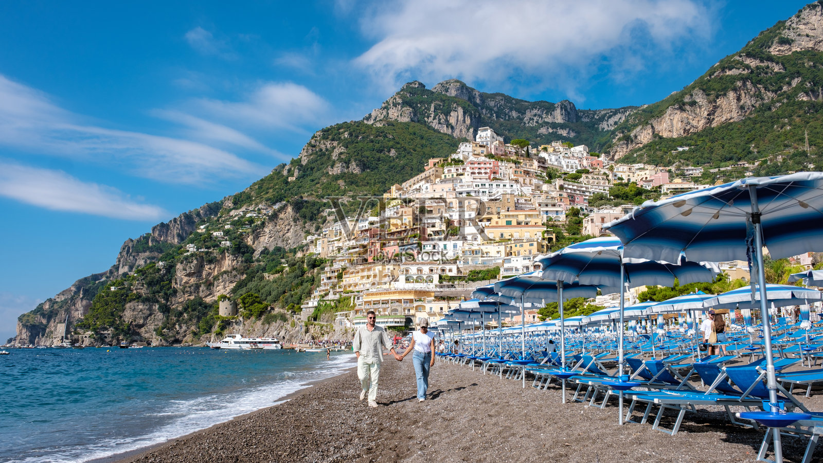 在阳光明媚的日子里,沿着阿马尔菲海岸的沙滩漫步,背景是五彩斑斓的波西塔诺。照片摄影图片