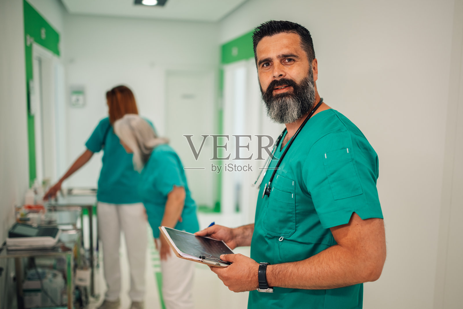 在医院走廊微笑的医生手持数字平板电脑。照片摄影图片