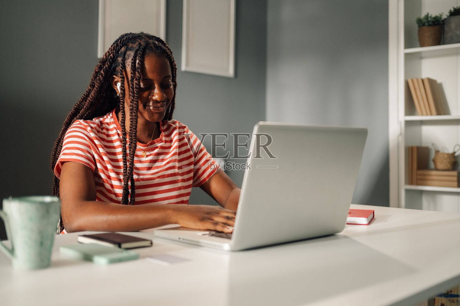 年轻的黑人女性在家中使用笔记本电脑和耳机工作照片摄影图片