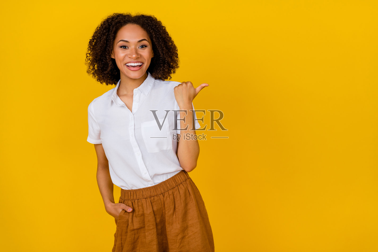 快乐漂亮的女性在黄色背景下推广优质服装店,指向空白区域。照片摄影图片