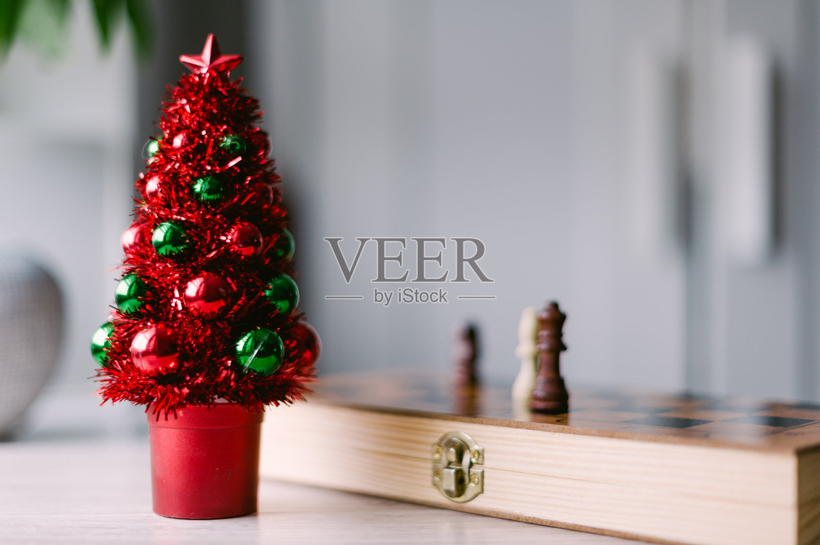 一棵红绿相间的圣诞树放在桌子上,旁边是一个国际象棋棋盘。照片摄影图片