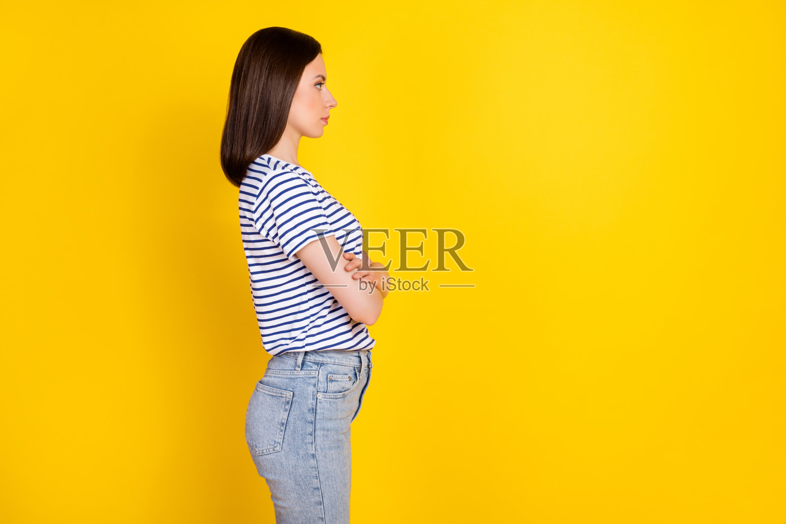 侧面肖像照片,迷人的漂亮女士交叉双臂,凝视空旷的空间,穿着条纹服装,背景为黄色。照片摄影图片