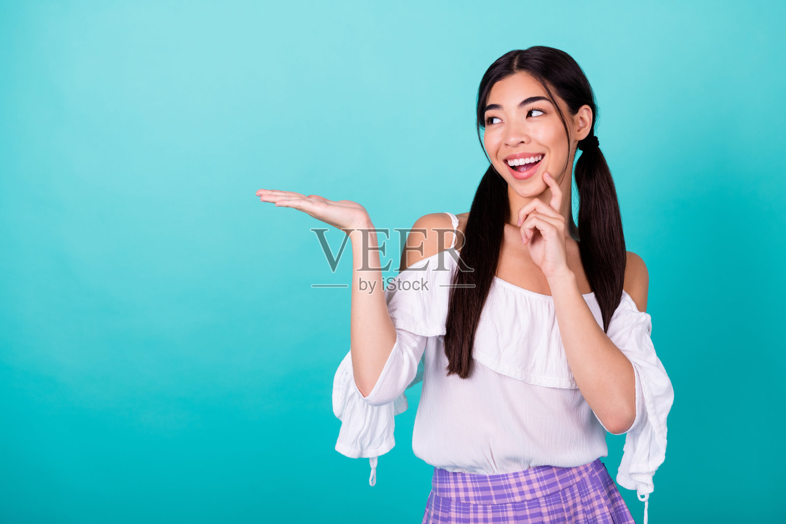 马来西亚美女的肖像,手指轻触下巴,手臂托住空旷的空间,背景为鲜艳的青绿色。照片摄影图片