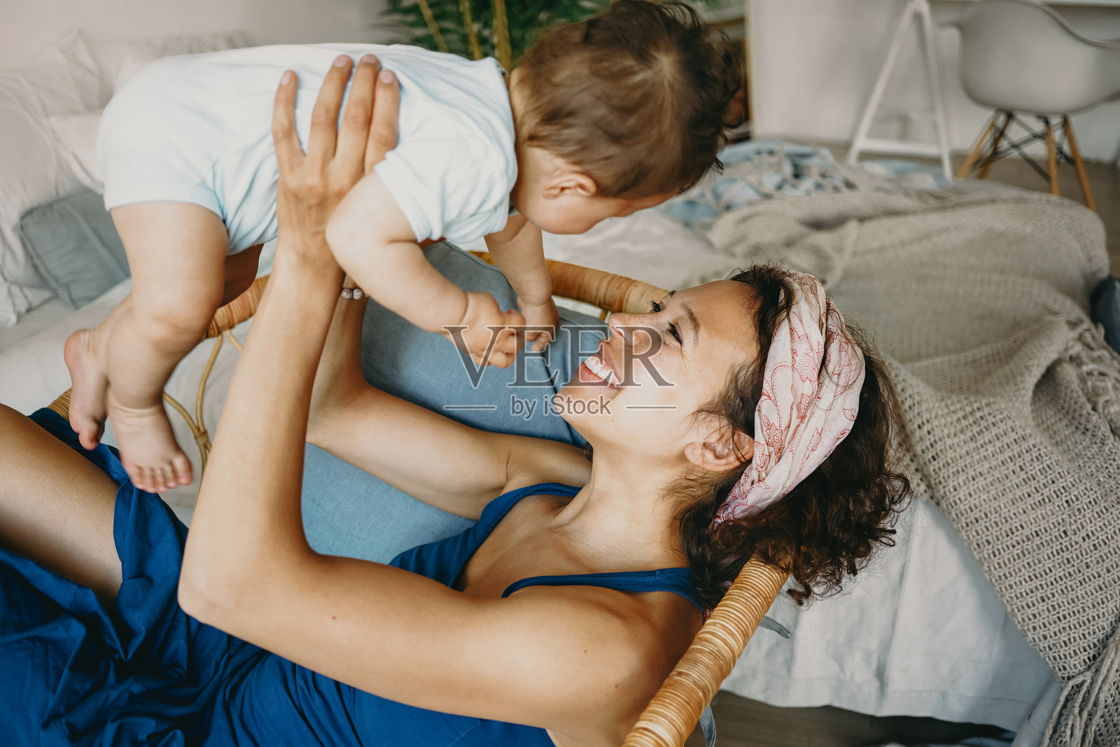 快乐无忧的童年。室内拍摄,一位美丽的年轻黑肤女性穿着休闲服,正在和她可爱的婴儿儿子玩耍,把他抛向空中,笑着,面带愉快的表情。照片摄影图片