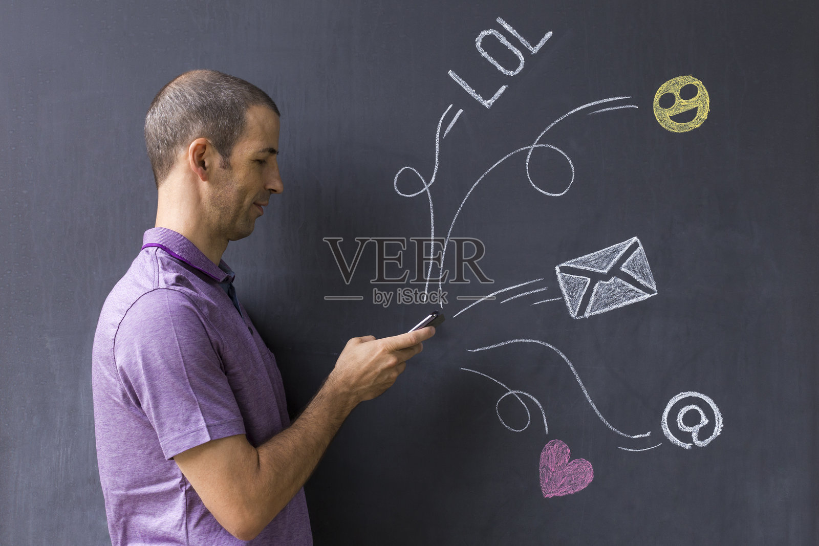 侧面视图的男子站在黑板旁边使用手机,黑板上有各种图标照片摄影图片