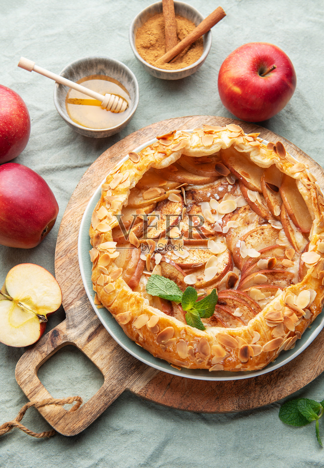 美味的自制苹果挞摆放在木板上,周围环绕着新鲜的苹果和蜂蜜。照片摄影图片