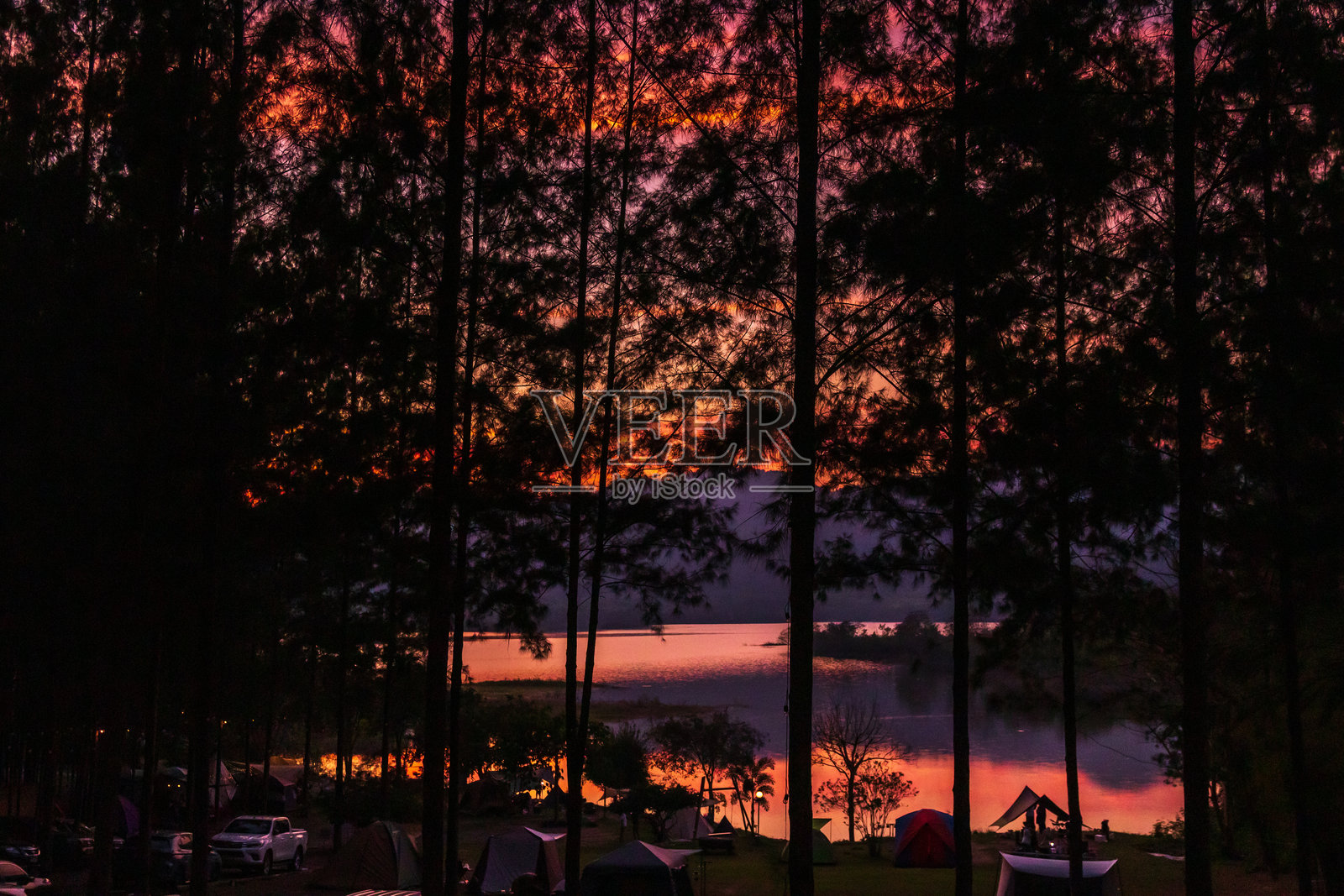 宁静的日落映照在平静的湖面上,周围高大的树木勾勒出一个宁静的露营氛围。照片摄影图片