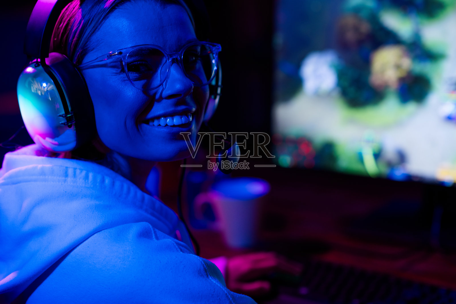 可爱的迷人金发女孩在室内紫蓝色霓虹灯下愉快地微笑,玩电脑游戏,深夜时分。照片摄影图片