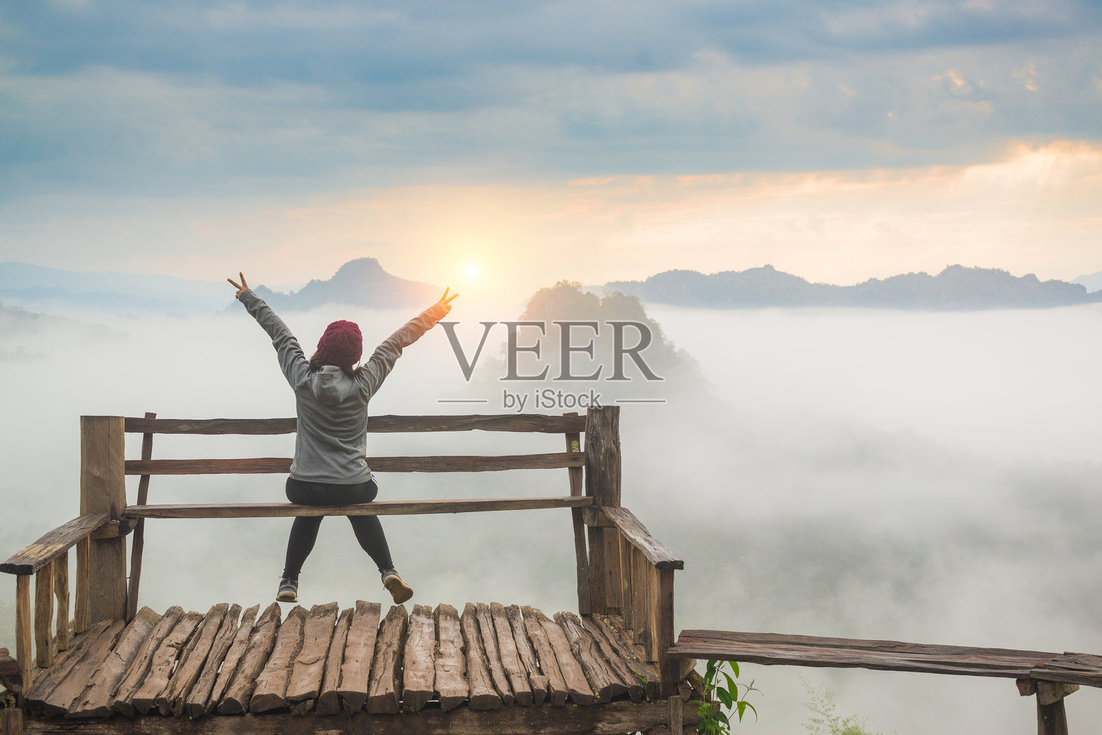 女人背对着天空坐着,双臂伸展。照片摄影图片