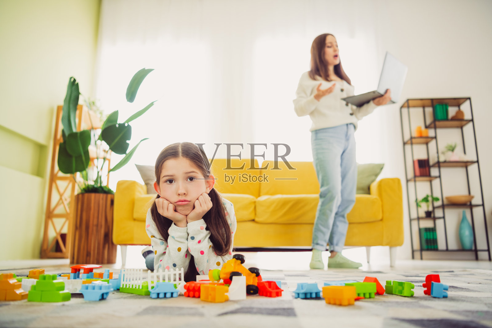 母亲在家工作,年轻女儿在客厅玩玩具。照片摄影图片