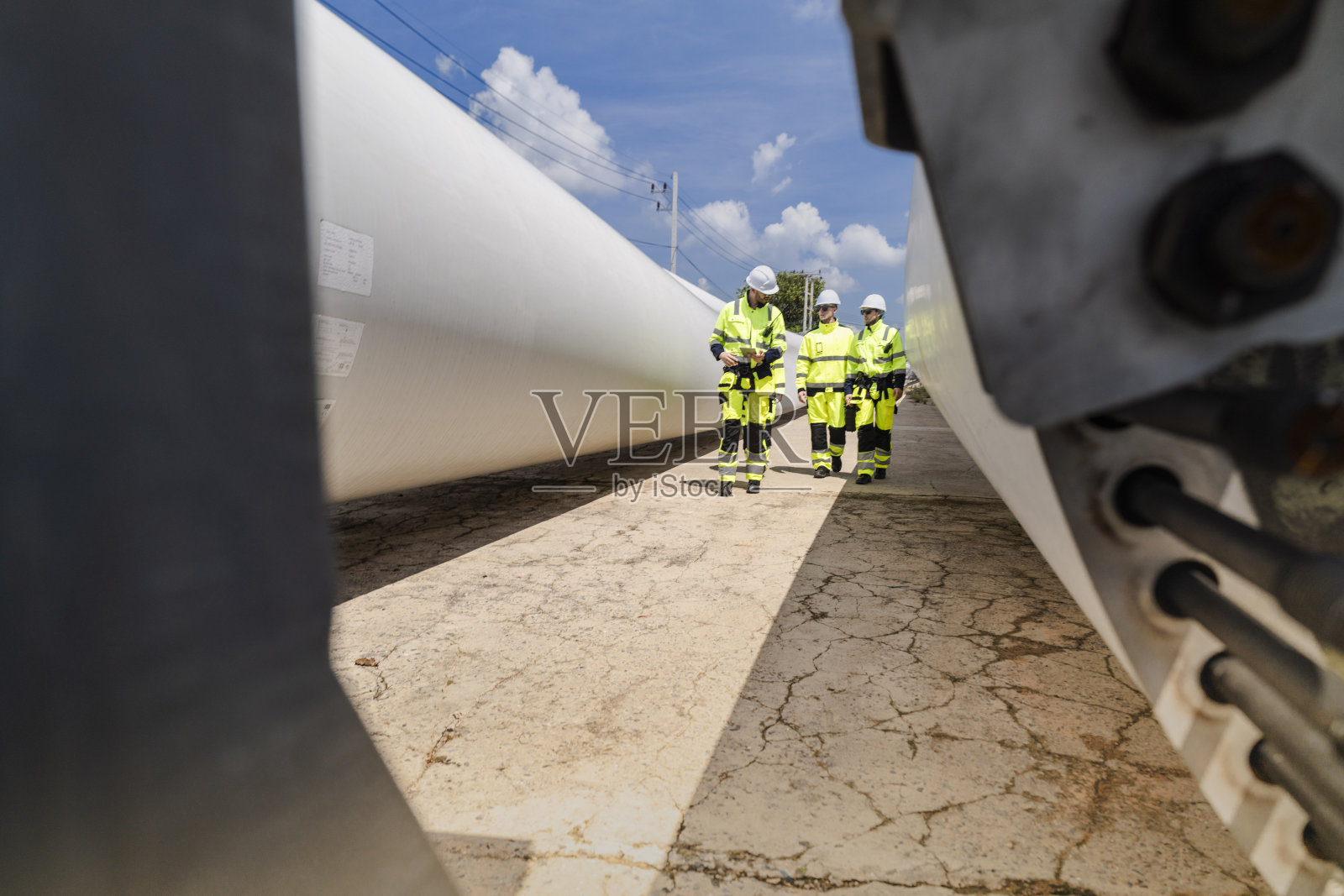 工程师们穿着高可视安全装备,在施工现场对风力涡轮机叶片进行详细检查。巨大的叶片躺在地面上,突显了可再生能源技术。照片摄影图片