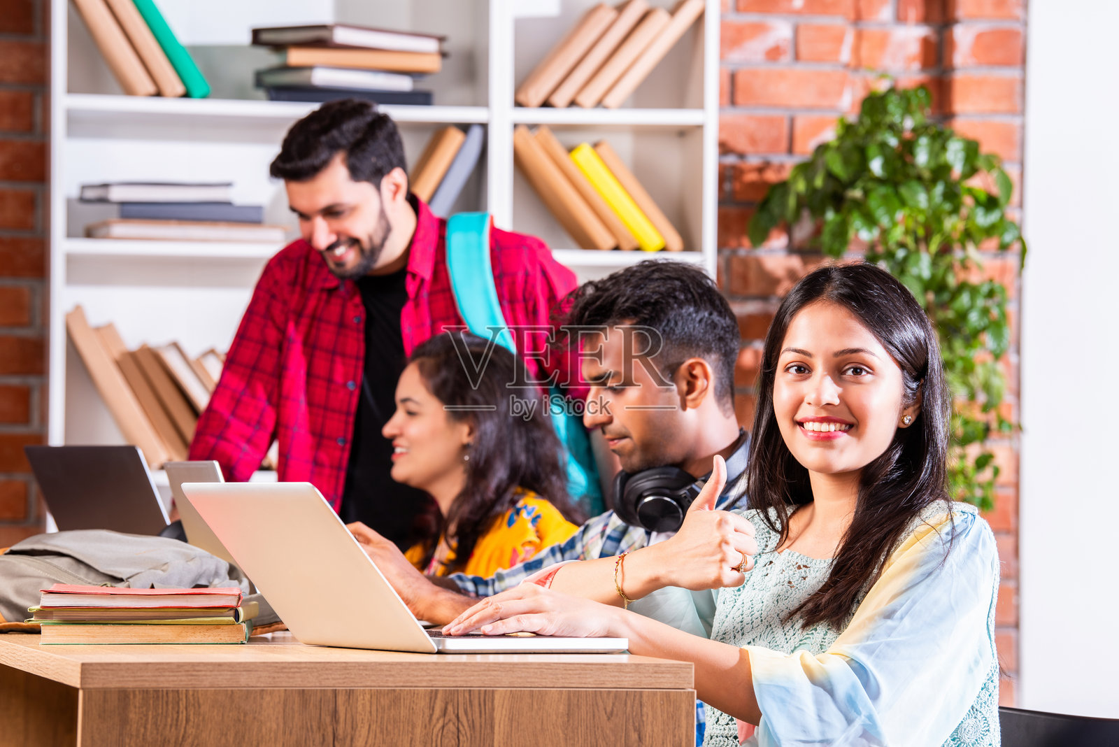 四个年轻的印度亚裔大学朋友带着背包,书,笔记本电脑,站在孤立的白色,在图书馆学习照片摄影图片