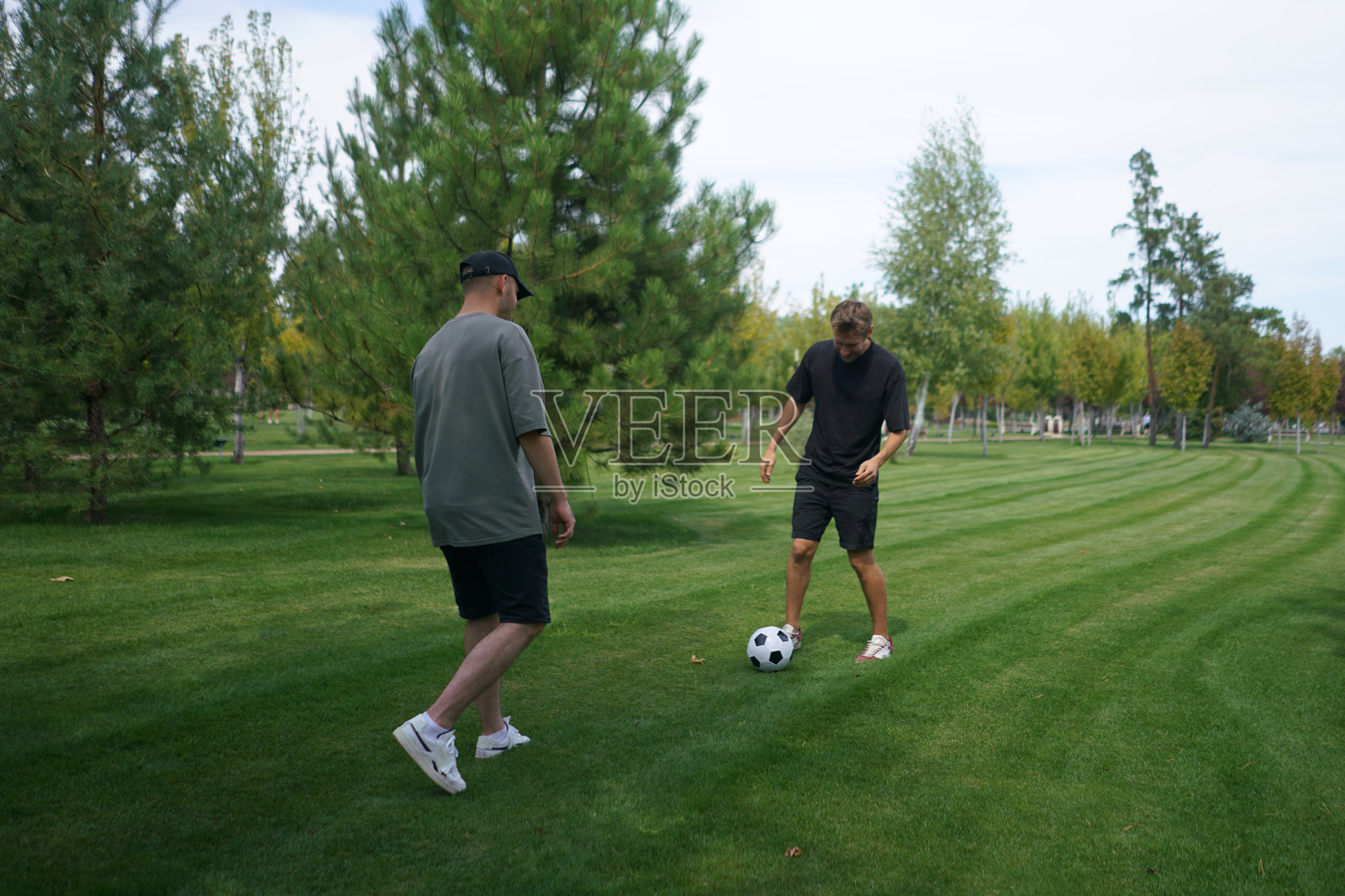 两个朋友在公园的郁郁葱葱的草坪上踢足球,练习技能,同时享受温暖的阳光和新鲜的空气。气氛轻松愉快。照片摄影图片