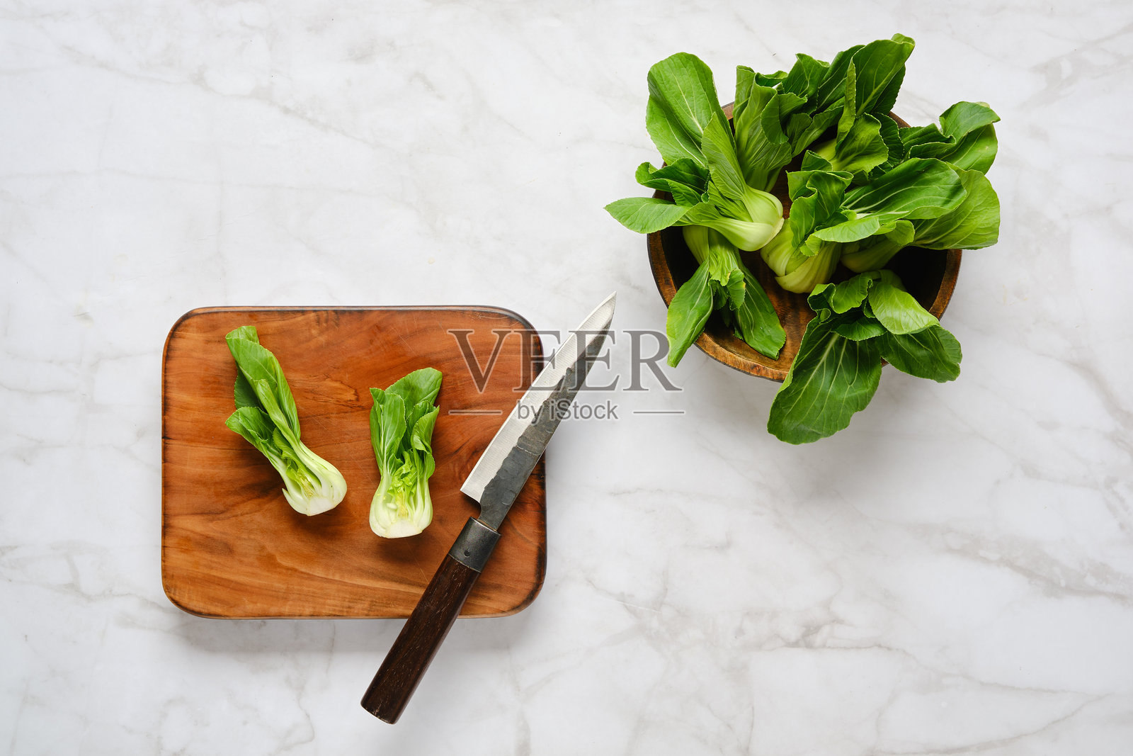 在木砧板上准备新鲜的小白菜,旁边有刀和其他绿叶蔬菜。照片摄影图片