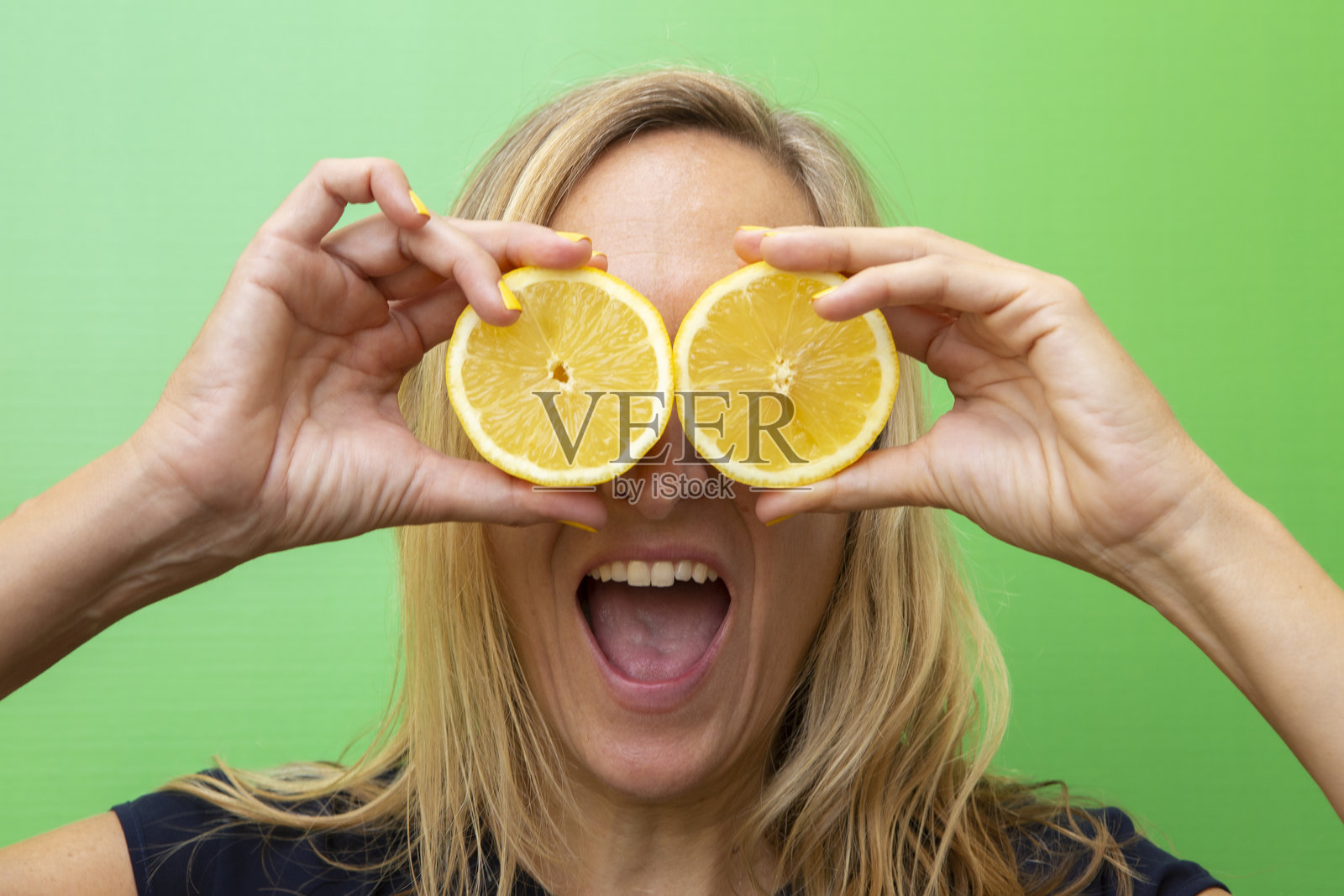 一位四十多岁的金发女性用两半柠檬遮住眼睛,嘴巴张开。照片摄影图片