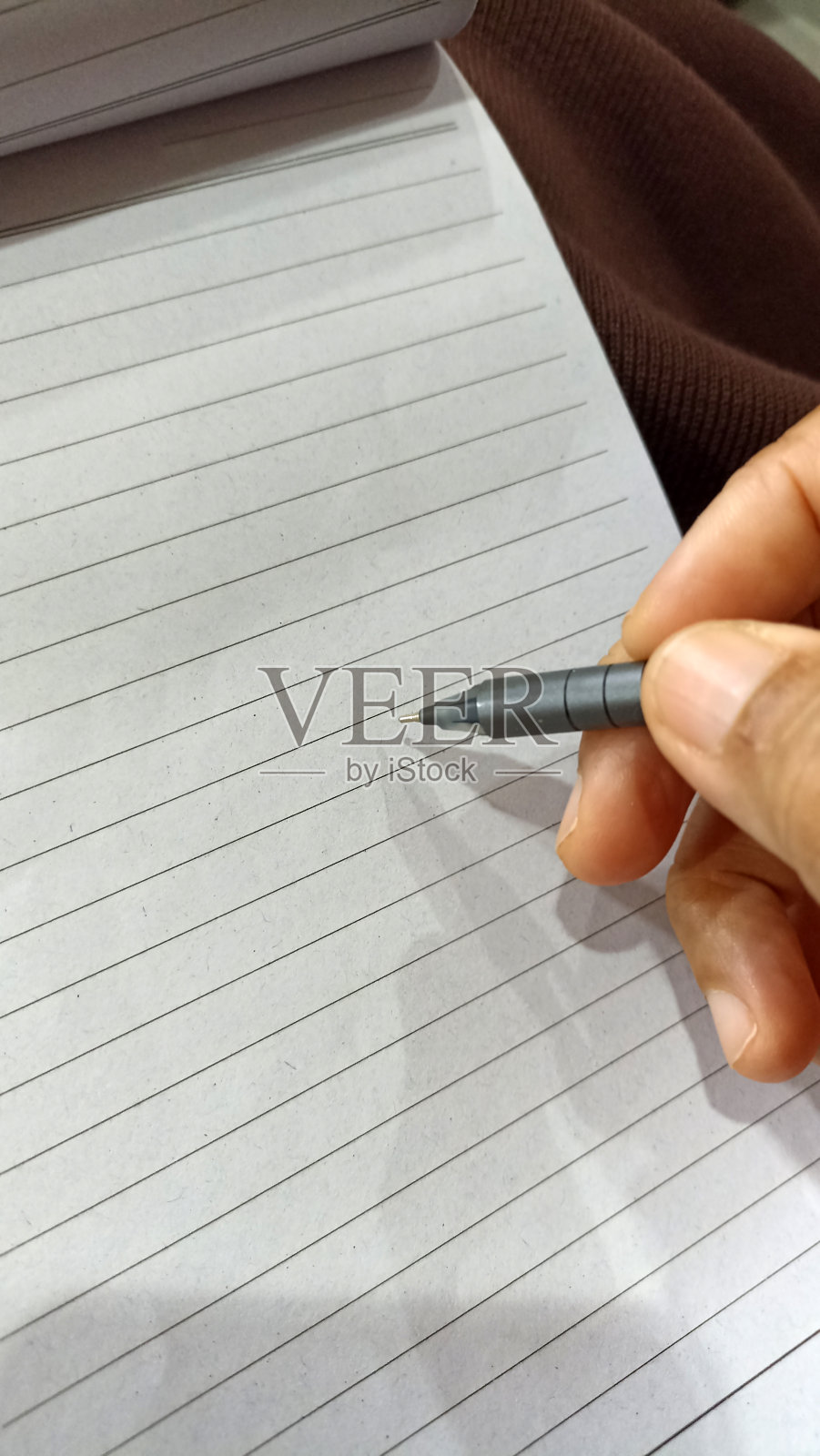 一个人的手拿着笔在空白笔记本上写字。照片摄影图片