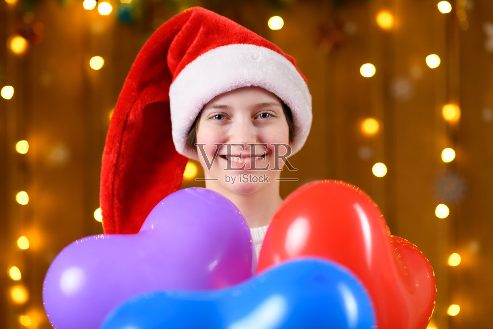 一名少女与红蓝心形气球合影,背景是新年节日装饰、灯光和花环。照片摄影图片