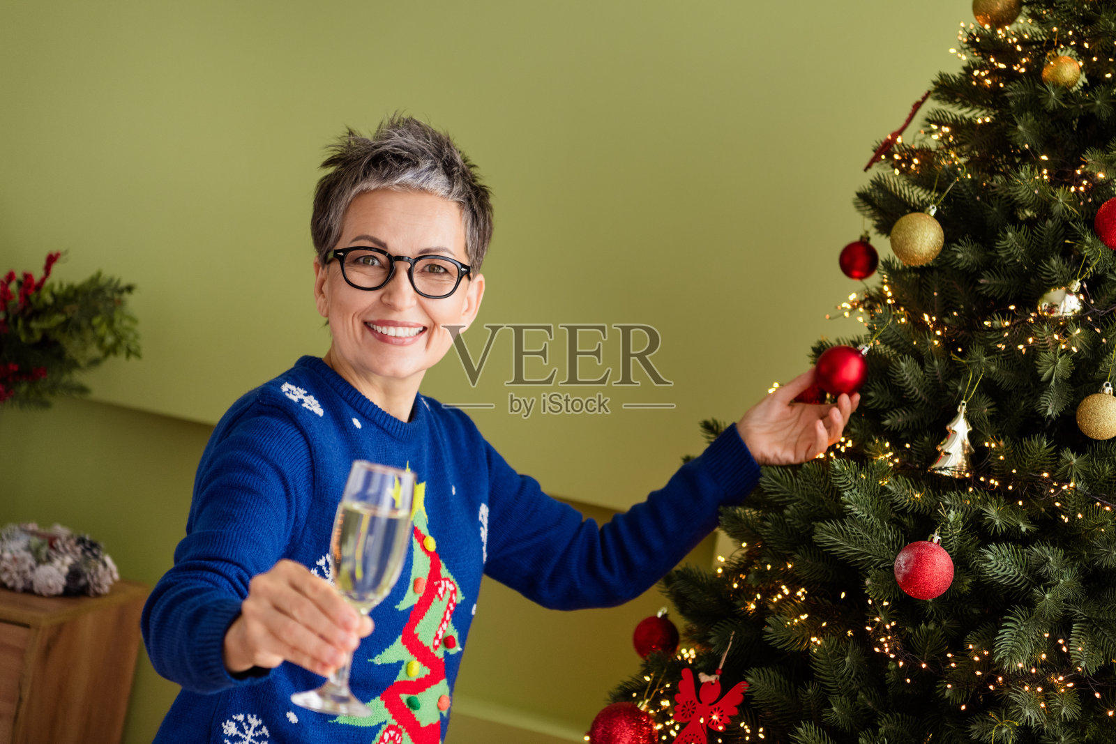 穿着蓝色衣服的可爱快乐女性在室内庆祝圣诞节,装饰着圣诞树迎接新年。照片摄影图片