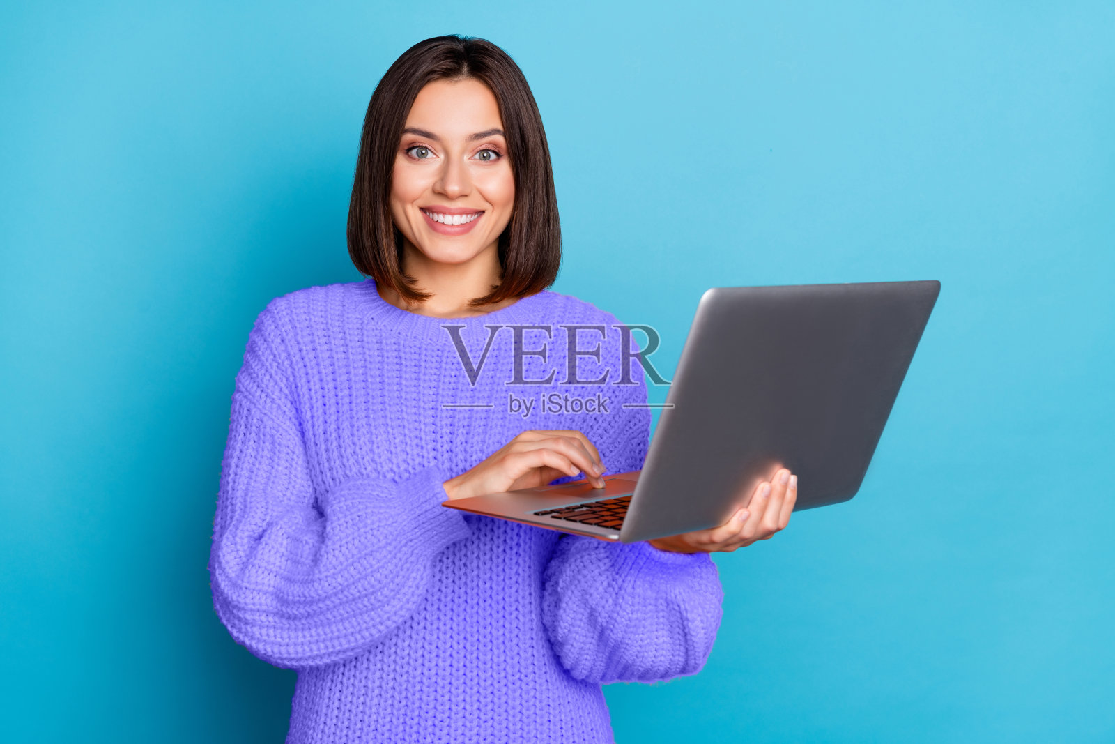 一位迷人、开朗的棕发女孩在明亮的蓝色背景下使用笔记本电脑开发项目的肖像照片摄影图片