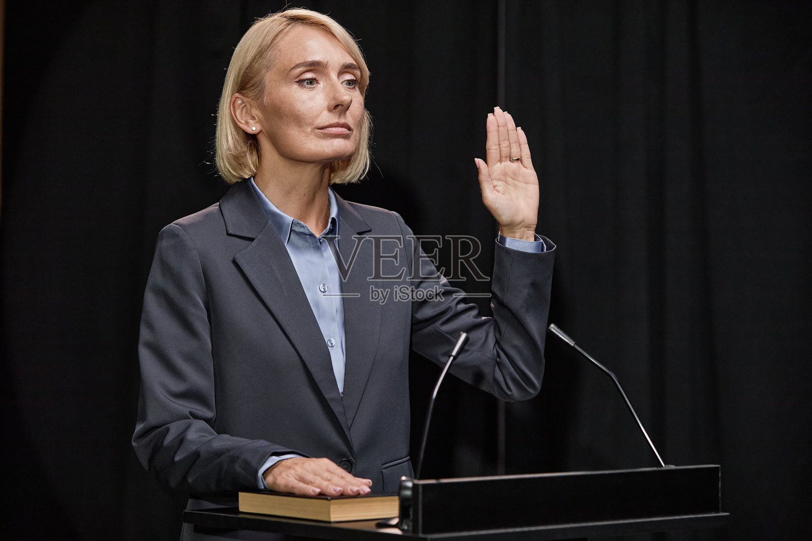 身穿蓝色西装的女性政治家在室内讲台上举手宣誓支持法律照片摄影图片