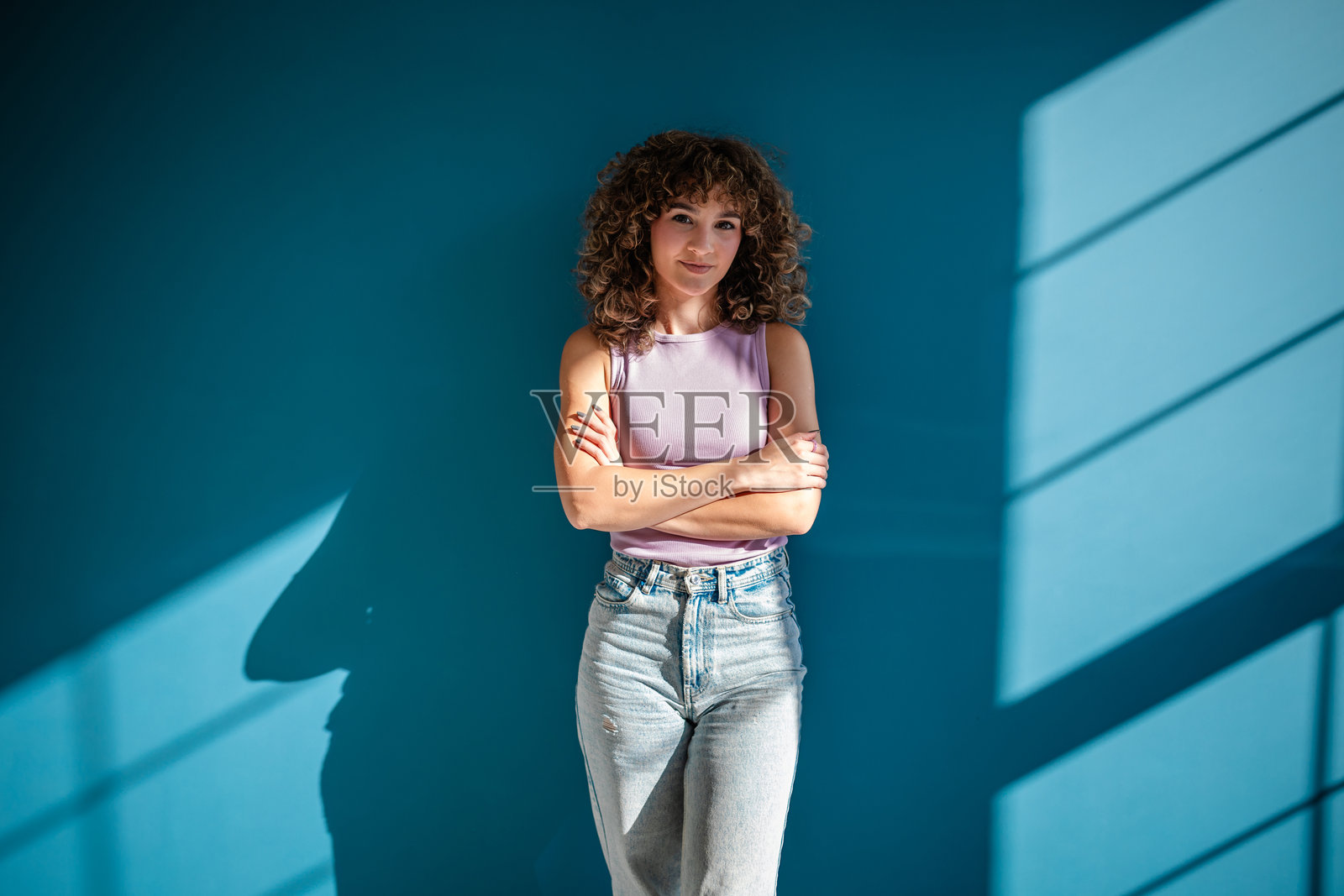 时尚女性站在蓝色墙壁前,沐浴在自然阳光下照片摄影图片