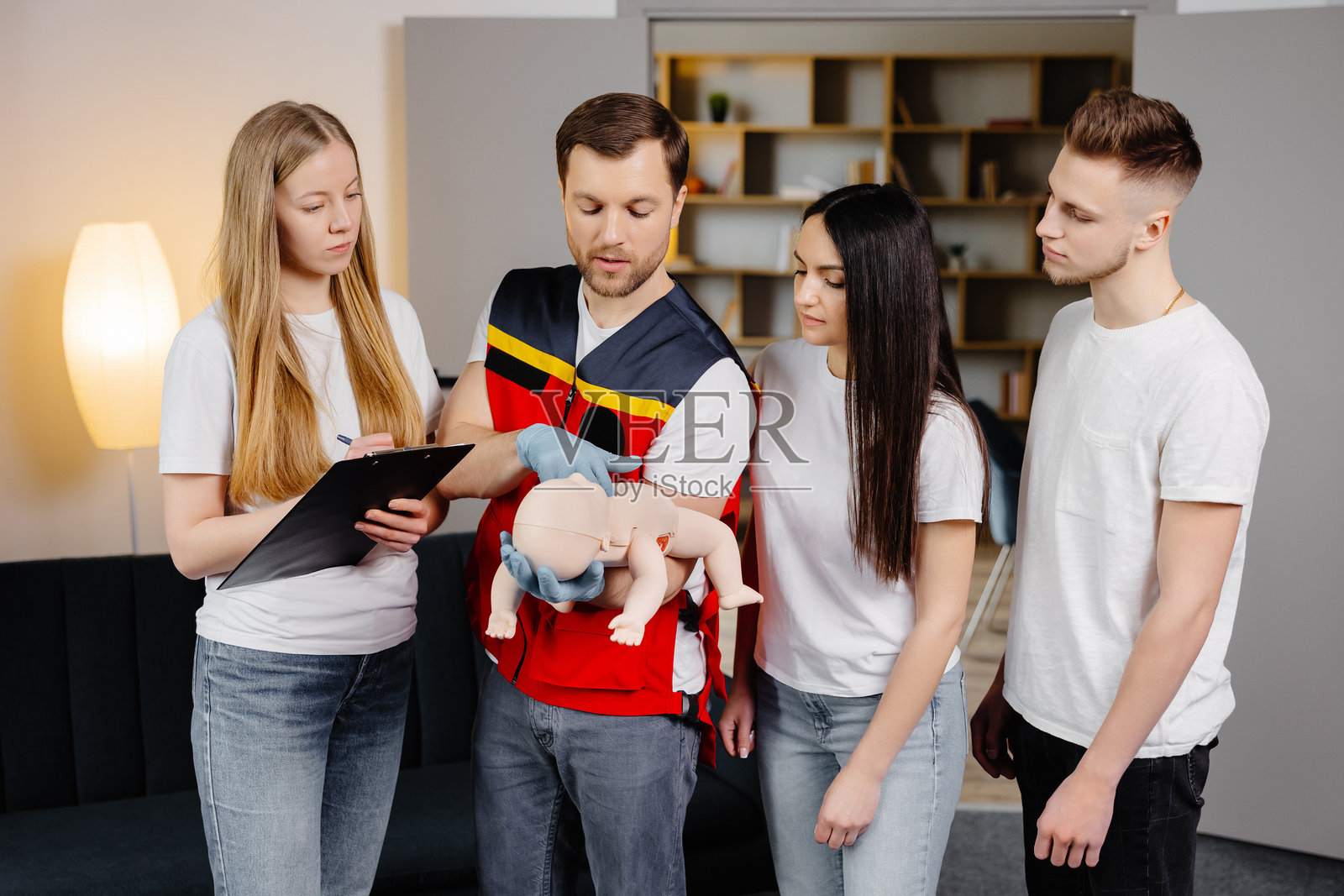一群人在室内培训中学习如何使用假人儿童进行急救。照片摄影图片