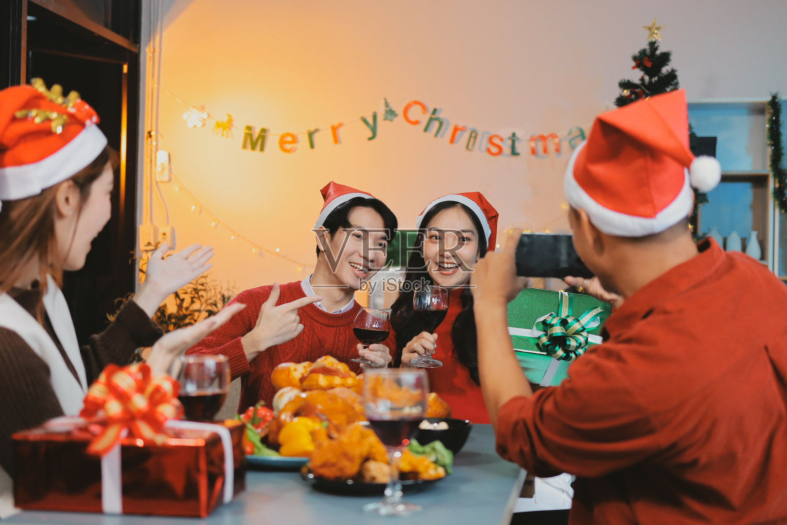 一群年轻的亚洲男女朋友在新年庆祝活动中玩得很开心,手里拿着礼物盒,站在装饰有圣诞树的地方,家中举行的午夜倒计时派对,庆祝节日季节。照片摄影图片