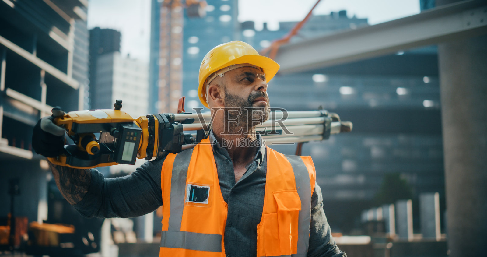 快乐的建筑工人手持测量仪,微笑着为相机摆姿势。专业的重工业工程师穿着安全橙色工作服和防护安全帽。照片摄影图片