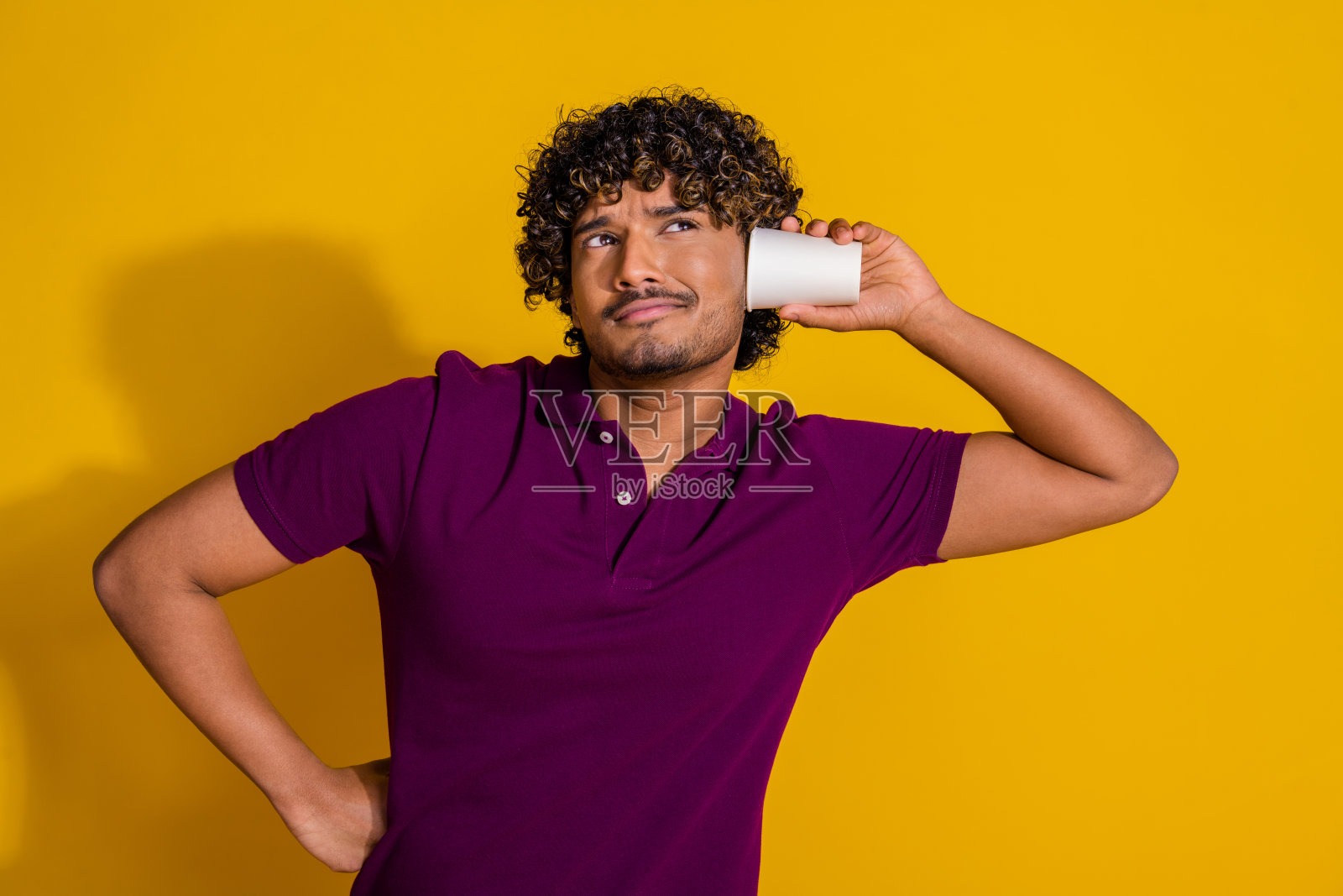 年轻男子穿着时尚的紫色服装,手持手机,面带惊讶地倾听,背景为黄色。照片摄影图片