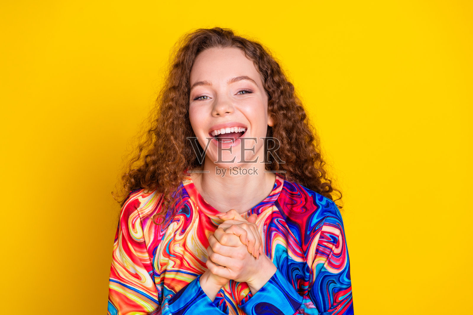 穿着时尚鲜艳服装的快乐年轻女性,拥有卷曲的红发,背景为明亮的黄色。照片摄影图片