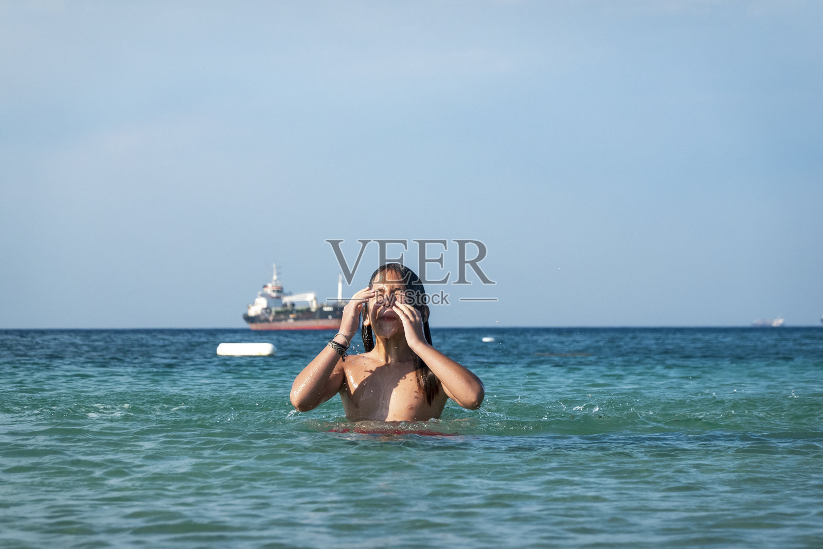 他在海里用手溅水。一个夏天的早晨。特内多斯。北爱琴海。12岁帅气的男孩。长发。照片摄影图片