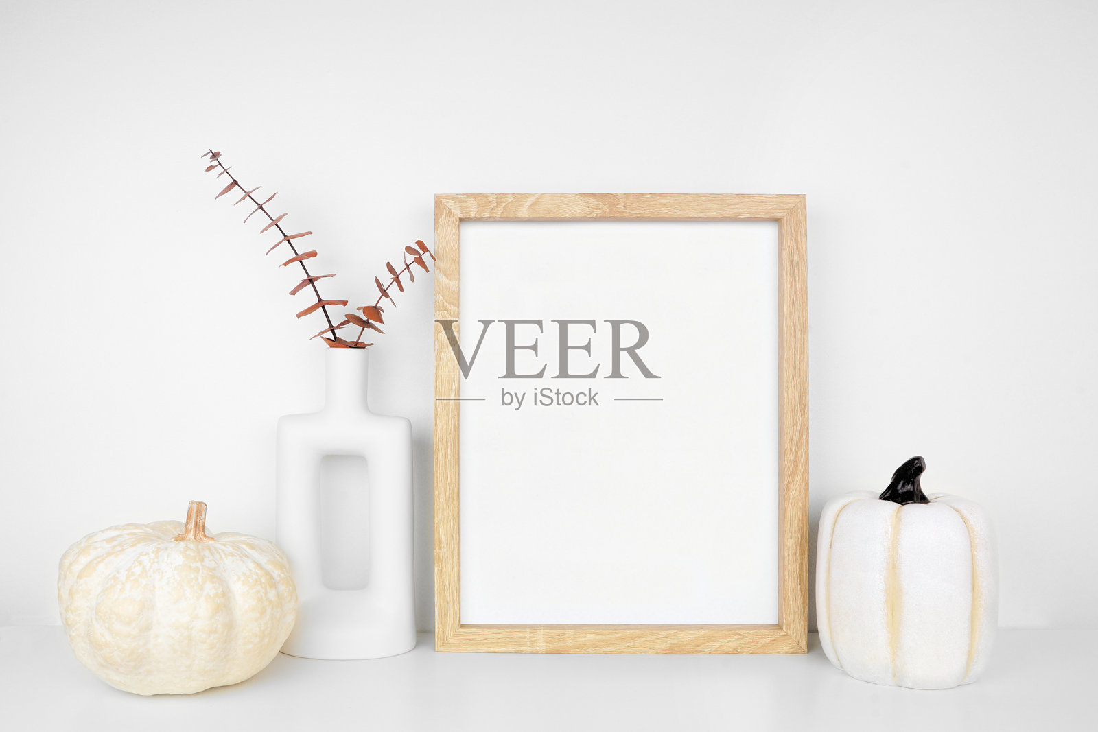 白色墙壁上的白色架子上摆放着带有秋季树枝和南瓜装饰的木质相框模型肖像照片摄影图片