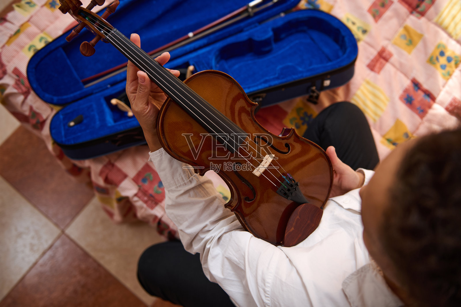 手持小提琴和蓝色琴盒的人,背景是五彩斑斓的毯子照片摄影图片