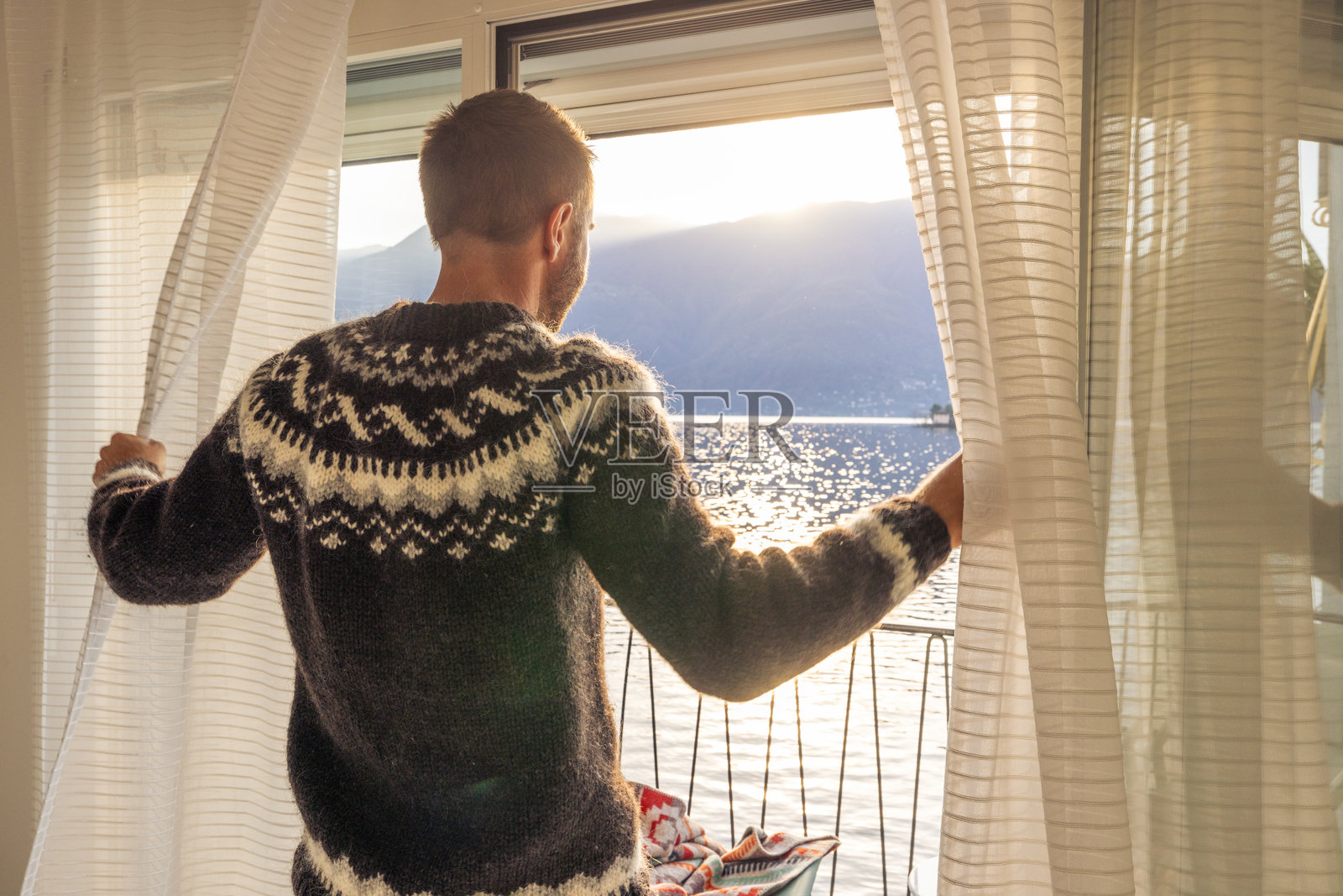 迎接新的一天:穿着毛衣的男人拉开窗帘,欣赏壮丽的湖景照片摄影图片