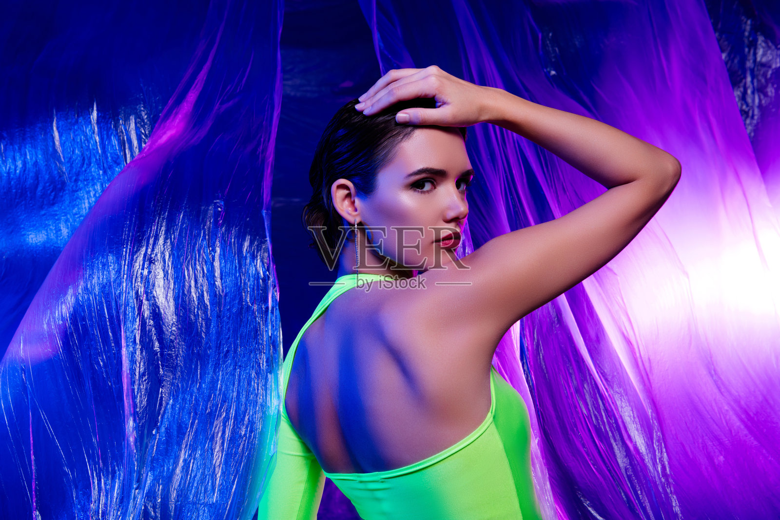 侧面站立的迷人女孩,手触头部,背景为生动的塑料色彩。照片摄影图片