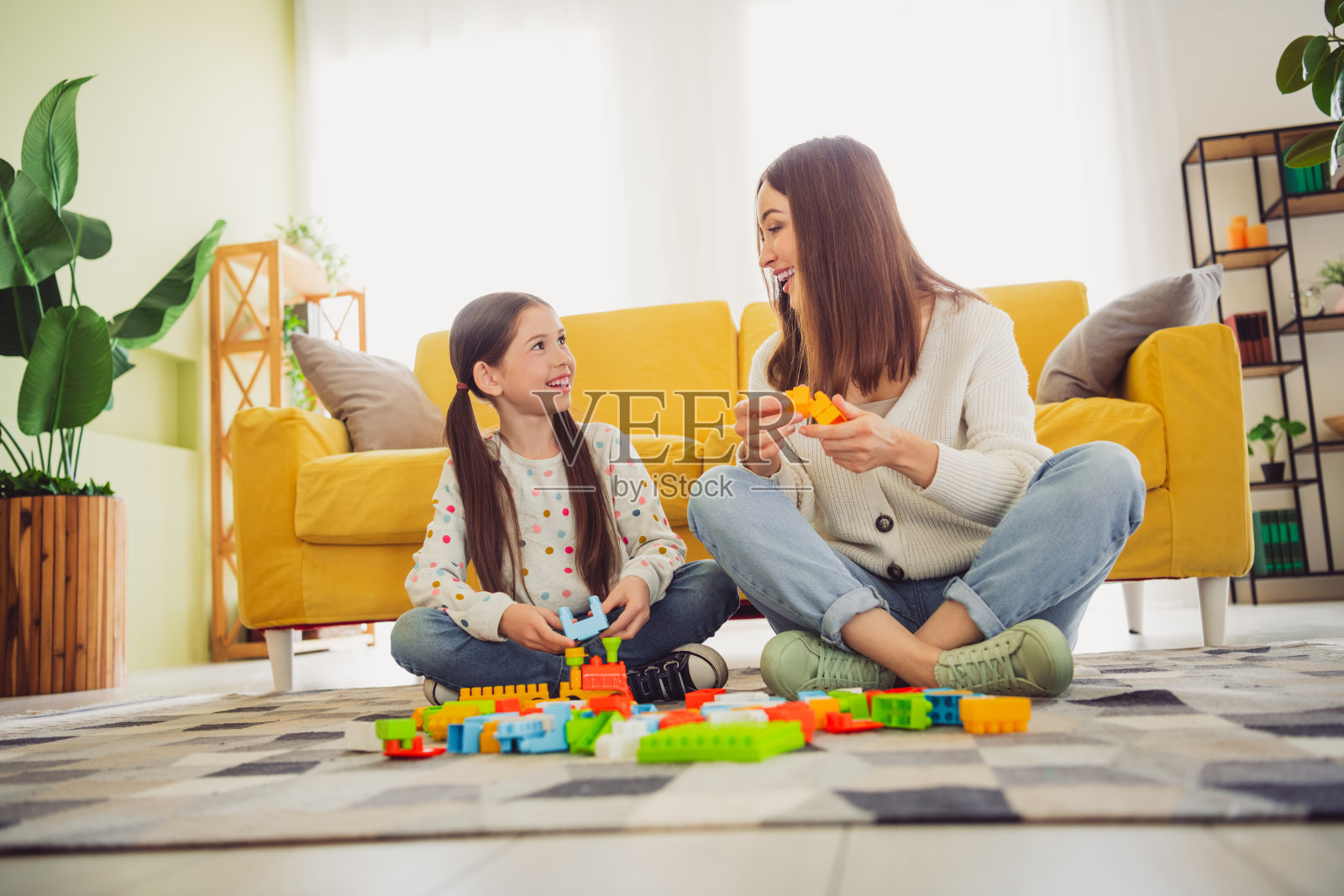 年轻母亲和女儿在温暖的春天里在家中亲密互动,享受在明亮的客厅里与玩具进行创意游戏的时光。照片摄影图片