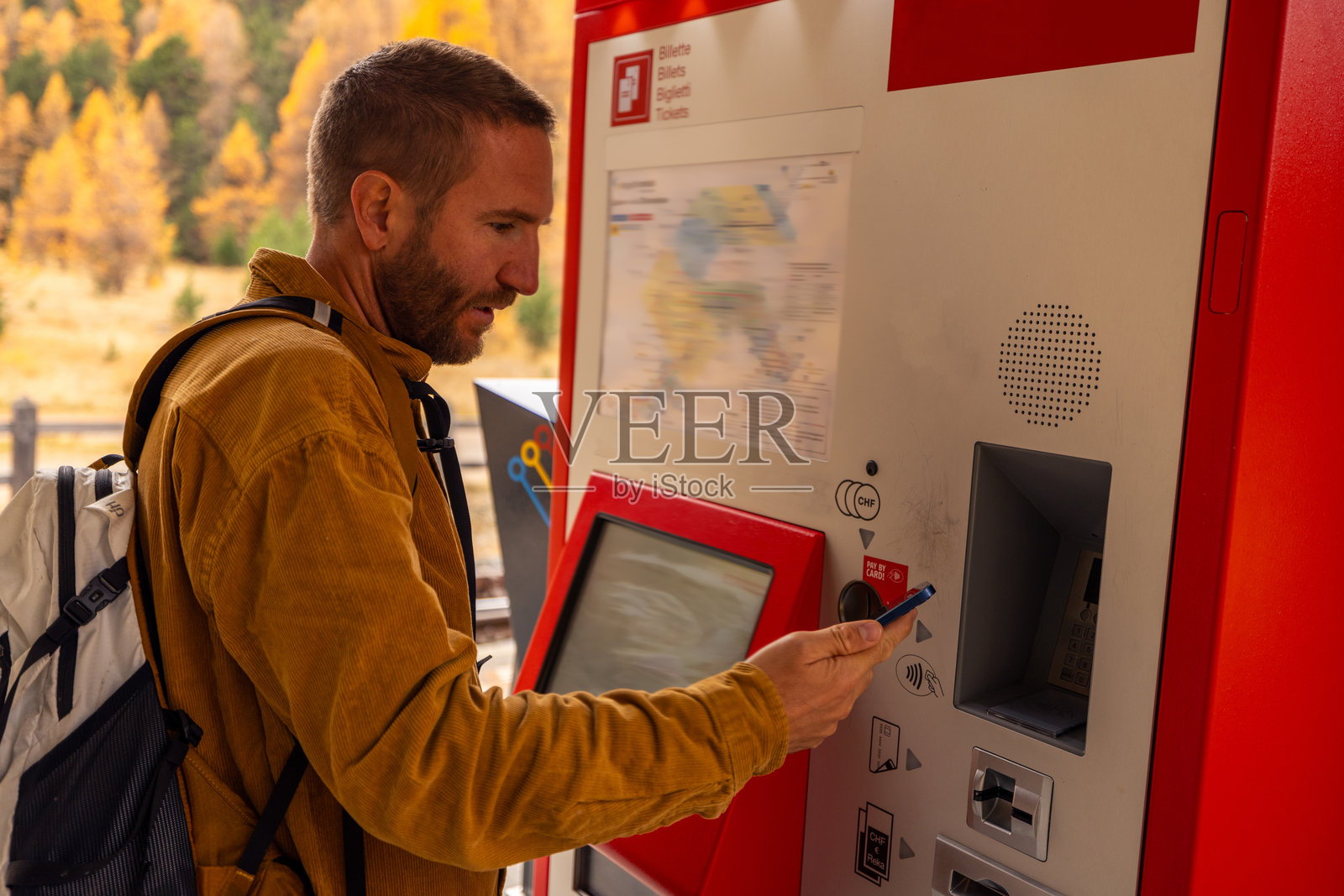 在火车站使用售票机的男子,他用手机付款照片摄影图片