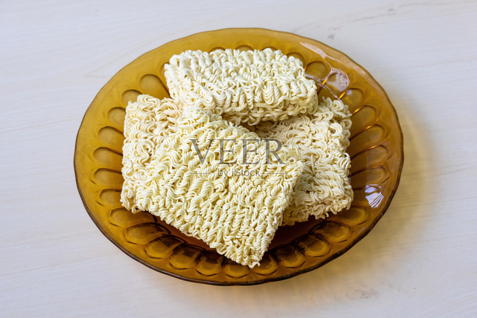 生的方便面放在玻璃盘子里,置于木质表面上。照片摄影图片