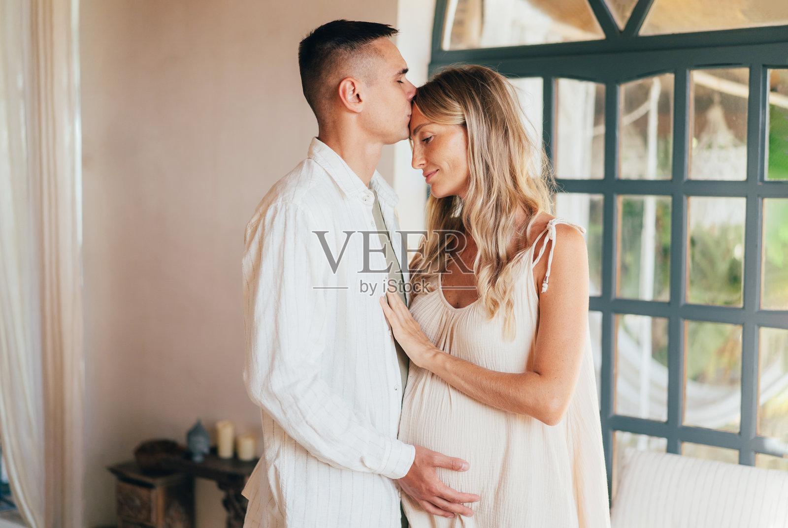 一对怀孕的情侣在室内相拥。照片摄影图片