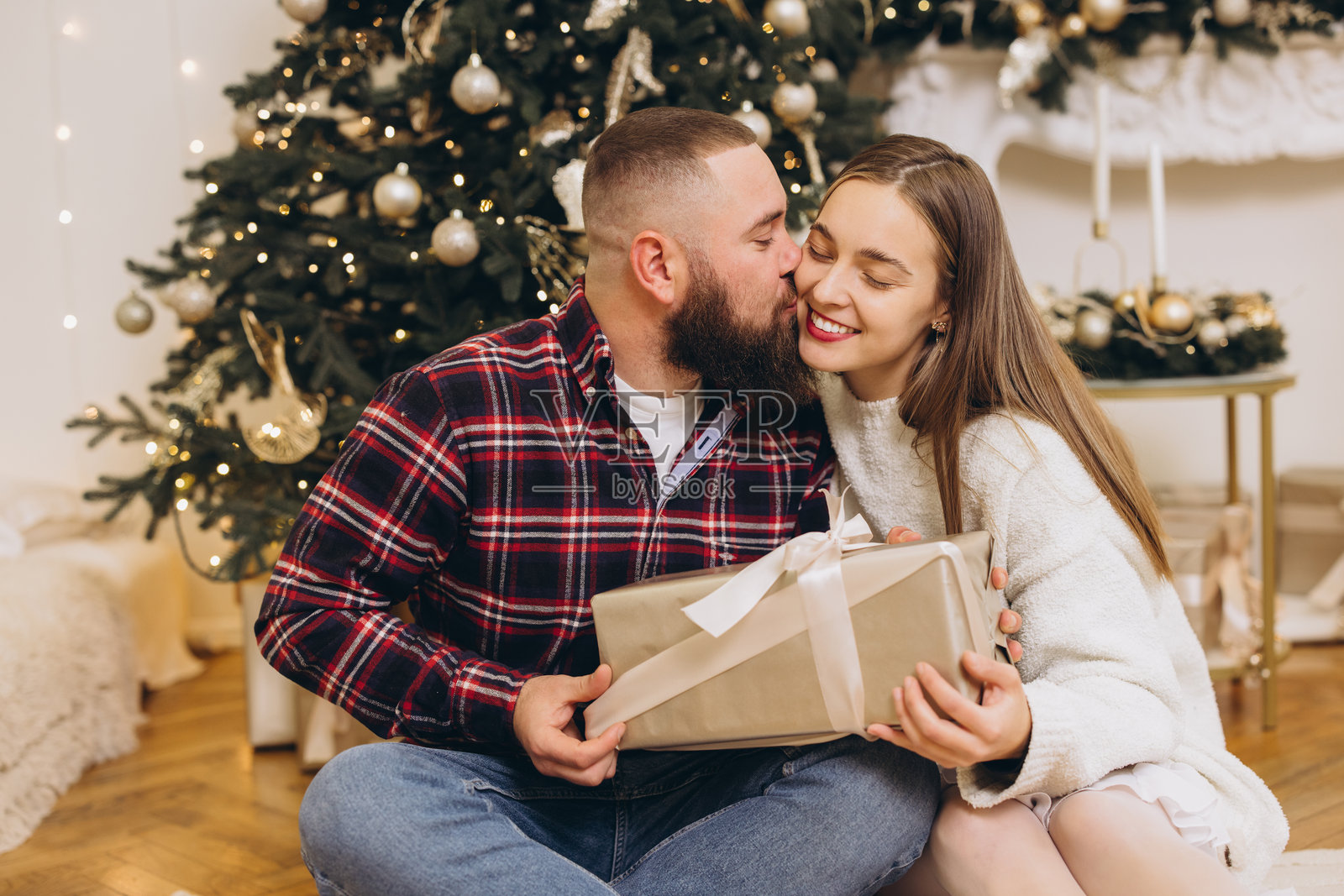 恩爱情侣在装饰好的圣诞树旁互赠礼物照片摄影图片