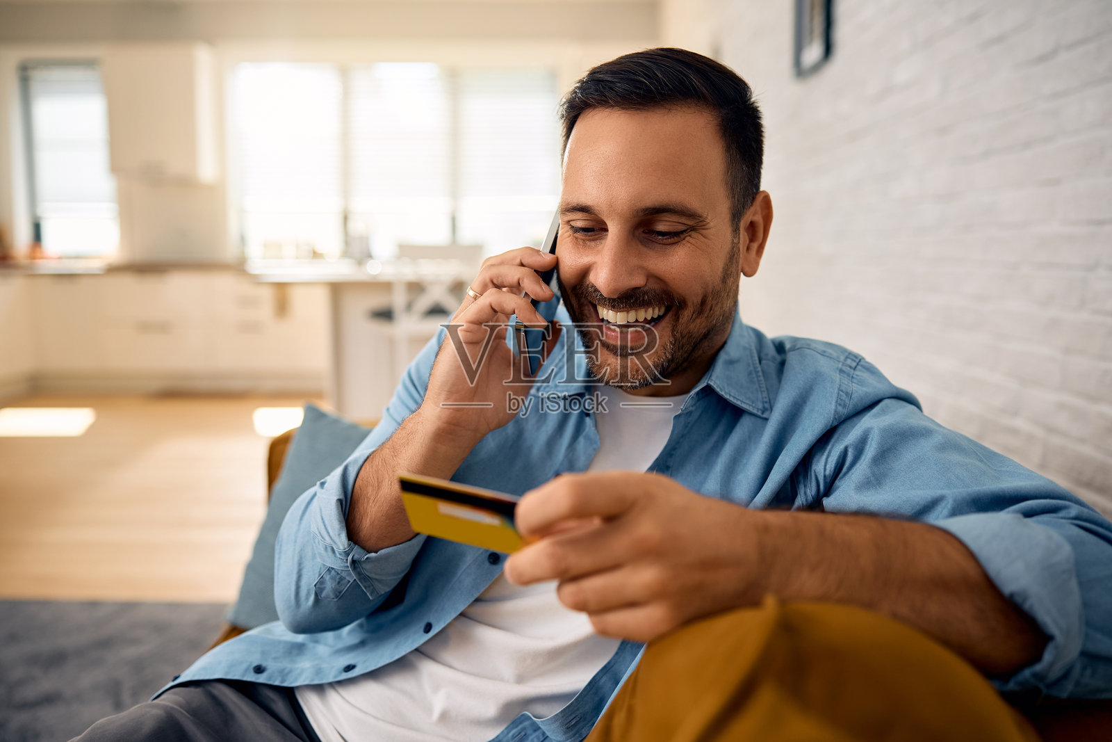 快乐的男人在家里一边打电话一边使用信用卡。照片摄影图片