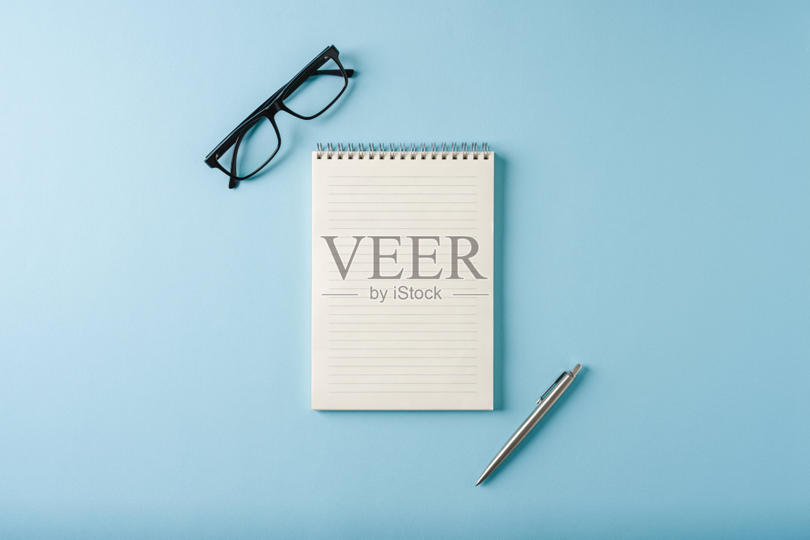 蓝色背景上的笔记本、眼镜和圆珠笔的俯视图照片摄影图片