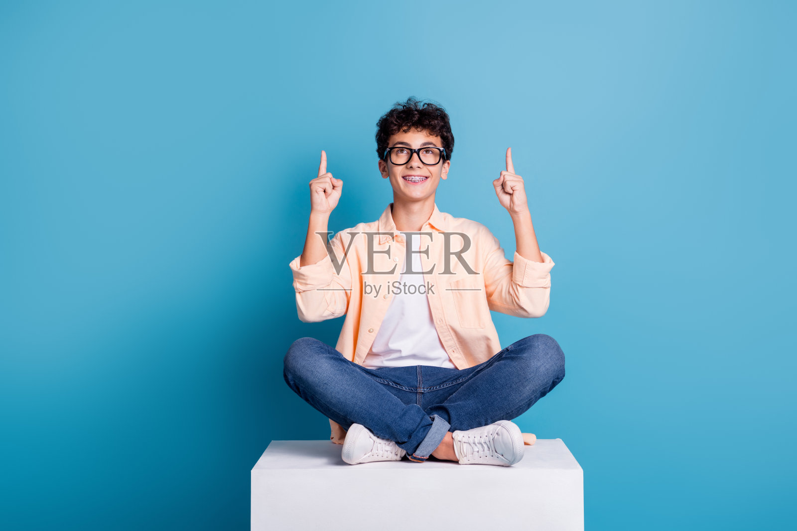 穿着时尚的年轻男子在充满活力的蓝色背景下指向上方,表达快乐和悠闲。照片摄影图片