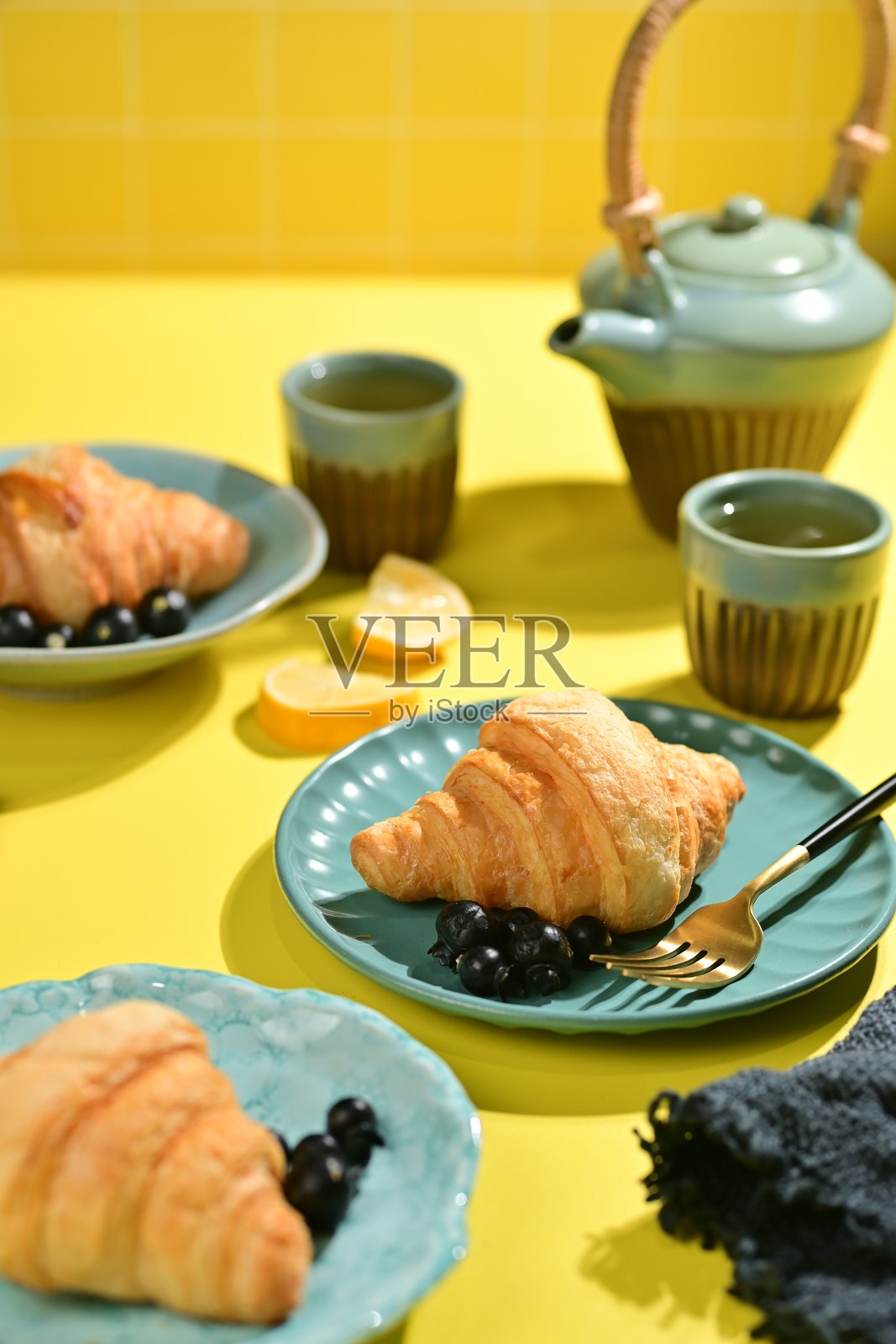 咖啡馆菜单:可颂 - 配有柠檬、蓝莓和茶,放在黄色桌子上,背景为纯黄色 - 食物造型照片摄影图片